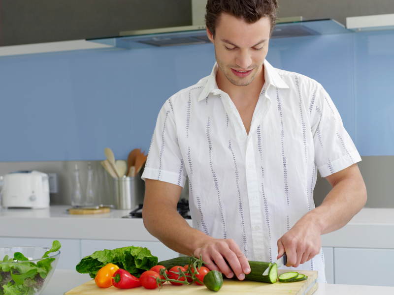 Young man cutting vegetables on wooden board in domestic kitchen