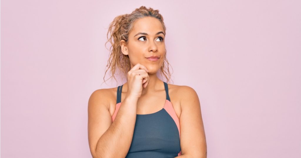 Closeup of a woman in an athletic top thinking against a pink wall.