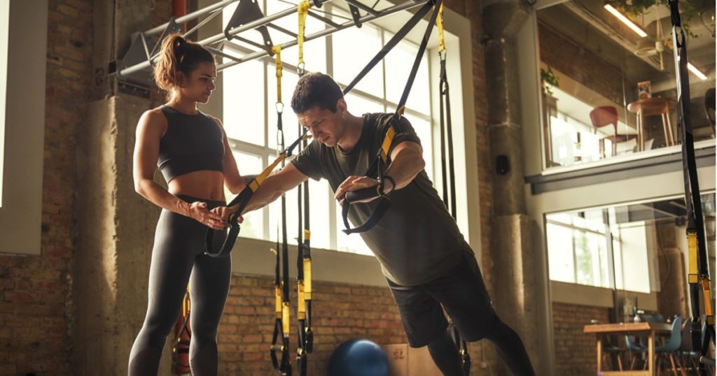 Personal trainer coaching a client through an exercise inside a gym.