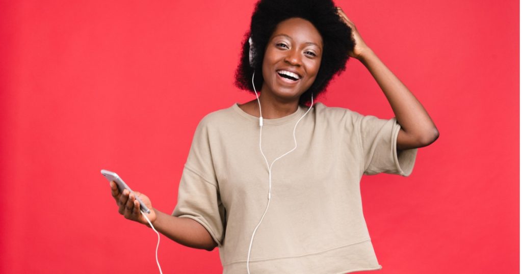 A photo of a woman set against a red background. The woman is using her smartphone to listen to music and dance. She does not have nomophobia or a smartphone addiction and doesn't need a digital detox.