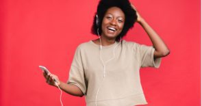 A photo of a woman set against a red background. The woman is using her smartphone to listen to music and dance. She does not have nomophobia or a smartphone addiction and doesn't need a digital detox.